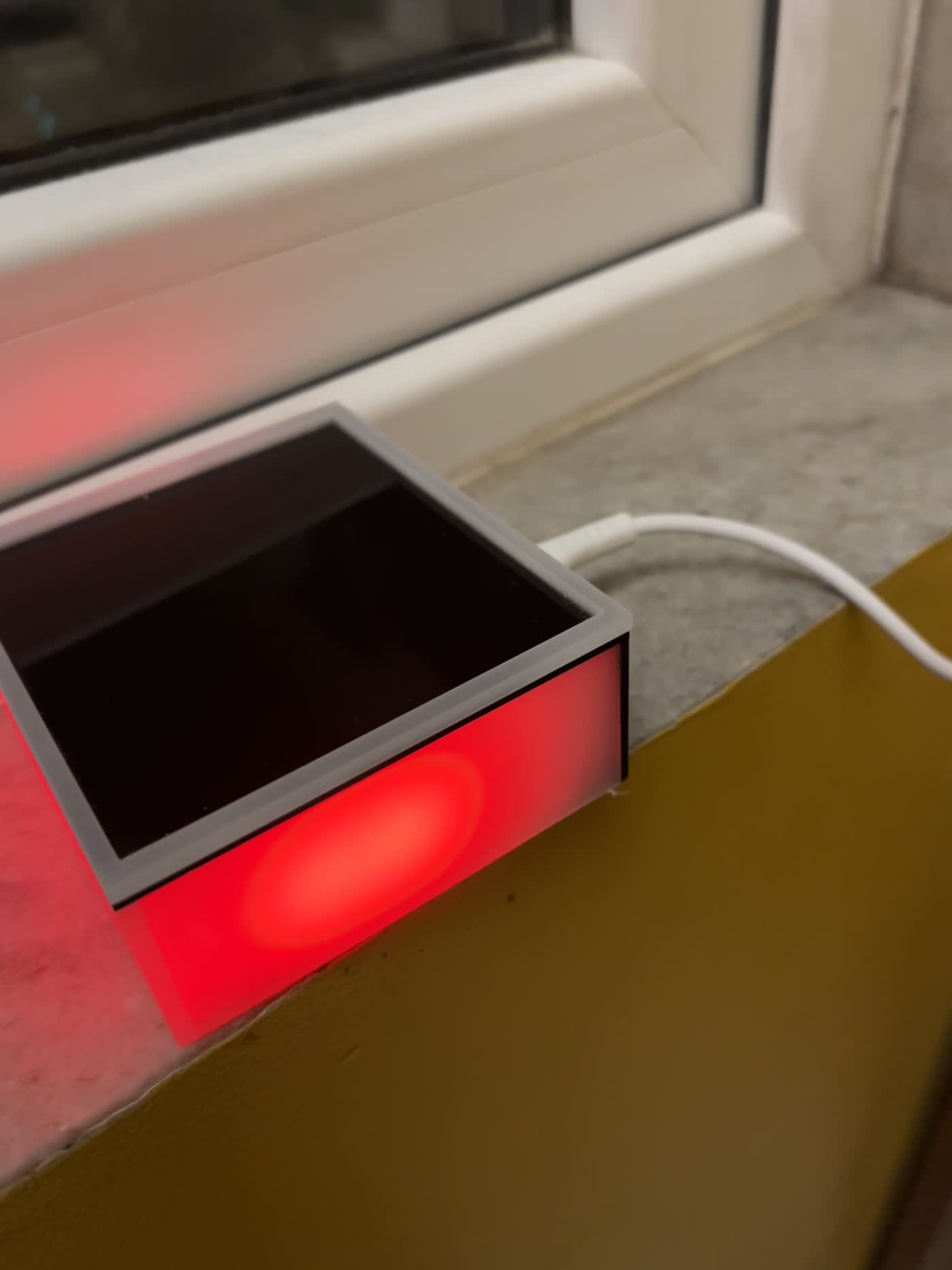 The newest Lumi prototype — a frosted enclosure with a dark mirrored lid, glowing red along its base on a windowsill.
